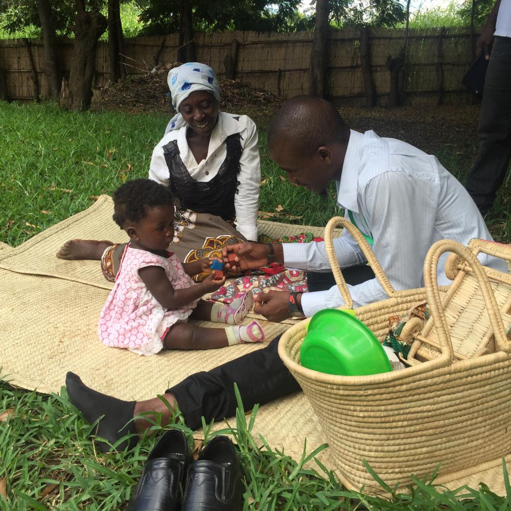 man and woman playing with small child on a blanket